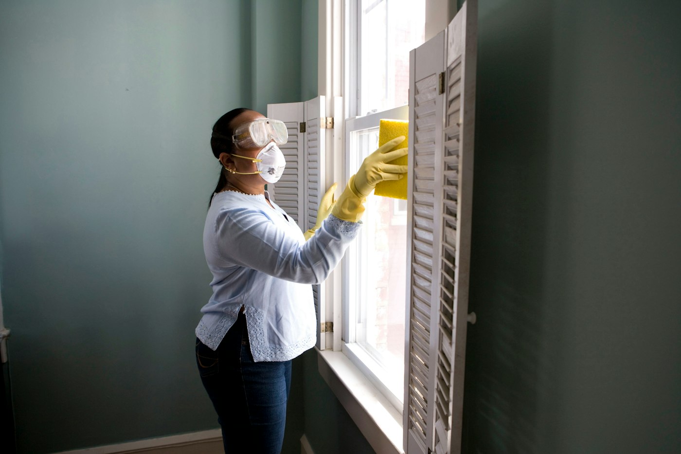 Schoonmaker met mondkapje en handschoenen maakt een raam schoon